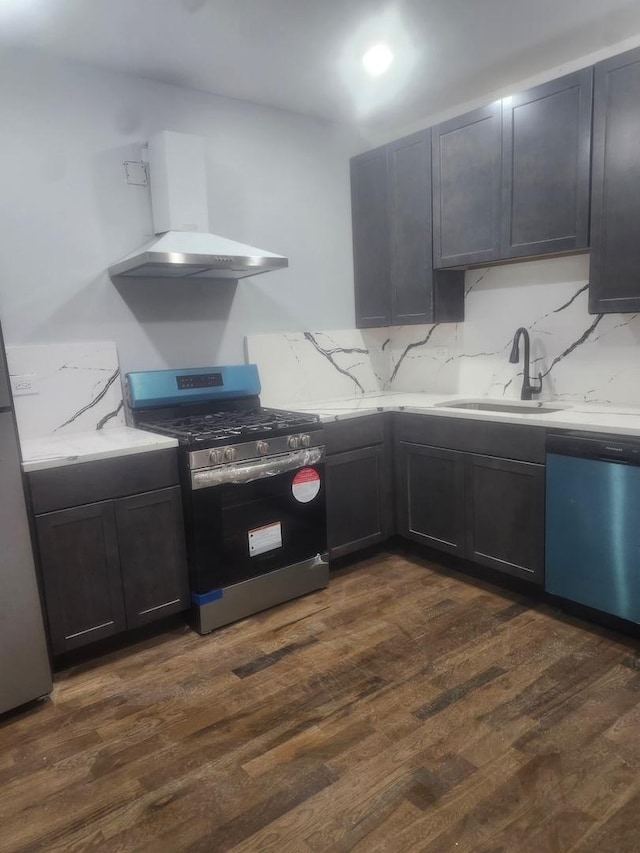 kitchen with dark wood-type flooring, appliances with stainless steel finishes, wall chimney range hood, and sink