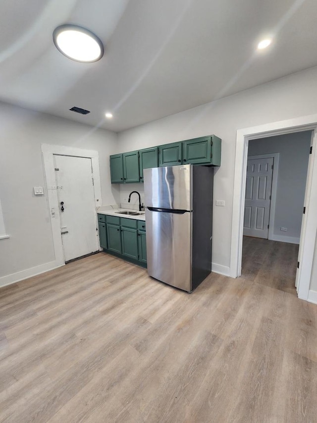 kitchen featuring light wood-type flooring, sink, stainless steel refrigerator, and green cabinets