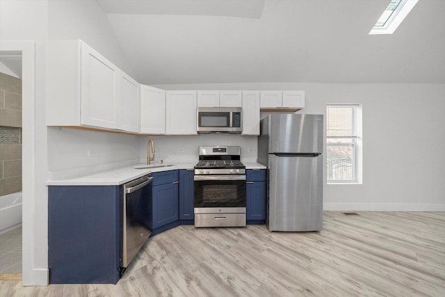 kitchen featuring lofted ceiling with skylight, sink, stainless steel appliances, white cabinets, and blue cabinets