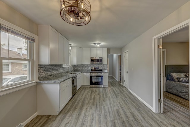 kitchen with white cabinetry, sink, light stone countertops, stainless steel appliances, and backsplash