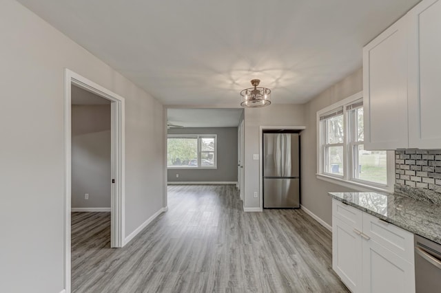 kitchen featuring white cabinetry, light stone countertops, tasteful backsplash, light hardwood / wood-style flooring, and appliances with stainless steel finishes