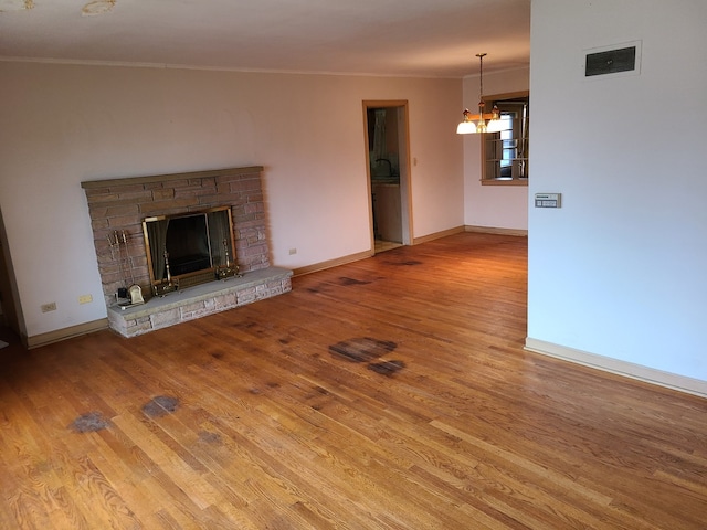 unfurnished living room featuring a stone fireplace, hardwood / wood-style flooring, ornamental molding, and a notable chandelier