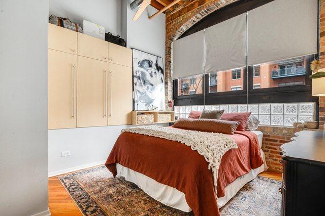 bedroom with multiple windows, brick wall, and light wood-type flooring