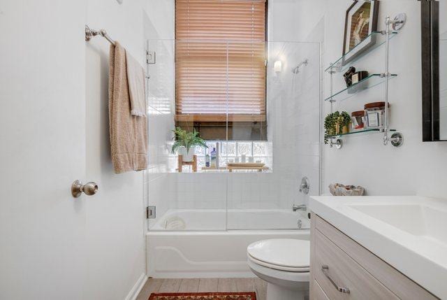 full bathroom with combined bath / shower with glass door, vanity, and toilet