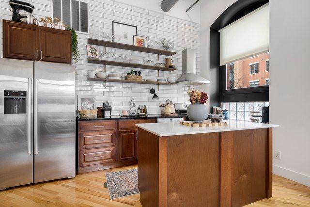 bar with stainless steel refrigerator with ice dispenser, tasteful backsplash, wall chimney exhaust hood, sink, and light hardwood / wood-style flooring