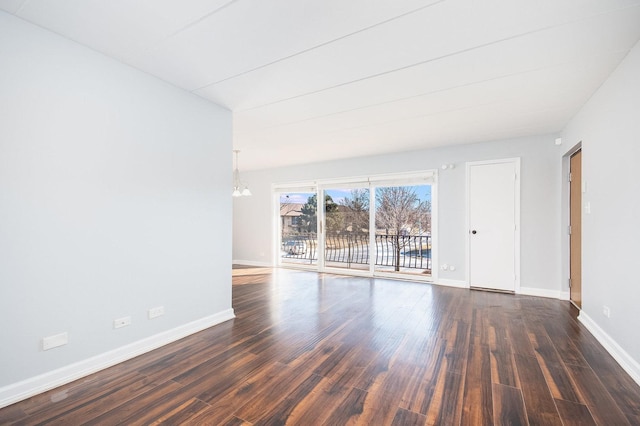 spare room with dark wood-type flooring and a chandelier