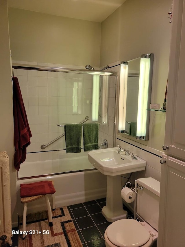 bathroom featuring tile patterned flooring, bath / shower combo with glass door, and toilet