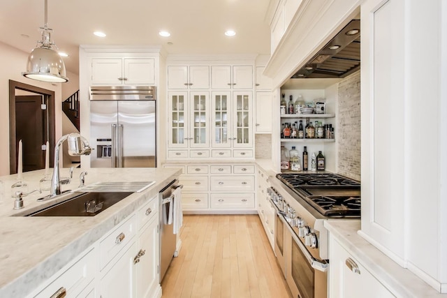 kitchen featuring sink, premium appliances, light stone countertops, white cabinets, and decorative light fixtures