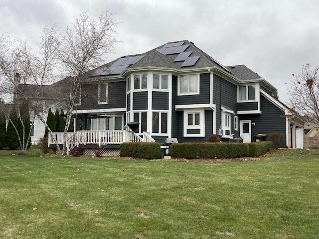 rear view of house with a yard, a deck, and solar panels