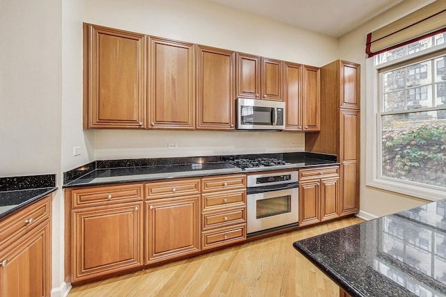 kitchen with dark stone countertops, light wood-type flooring, and stainless steel appliances