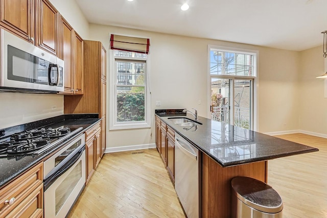 kitchen featuring a kitchen bar, stainless steel appliances, sink, light hardwood / wood-style flooring, and dark stone countertops