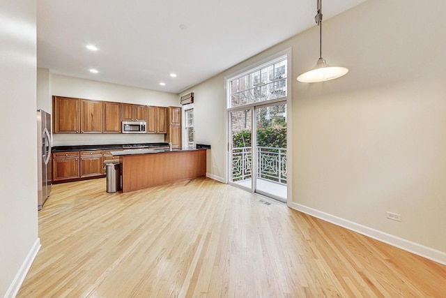 kitchen featuring light hardwood / wood-style flooring, kitchen peninsula, a towering ceiling, decorative light fixtures, and appliances with stainless steel finishes