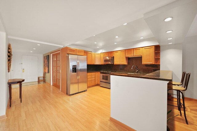 kitchen featuring a breakfast bar, dark stone countertops, light hardwood / wood-style floors, kitchen peninsula, and stainless steel appliances