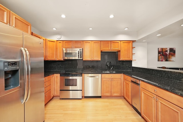 kitchen featuring backsplash, dark stone counters, sink, appliances with stainless steel finishes, and light hardwood / wood-style floors