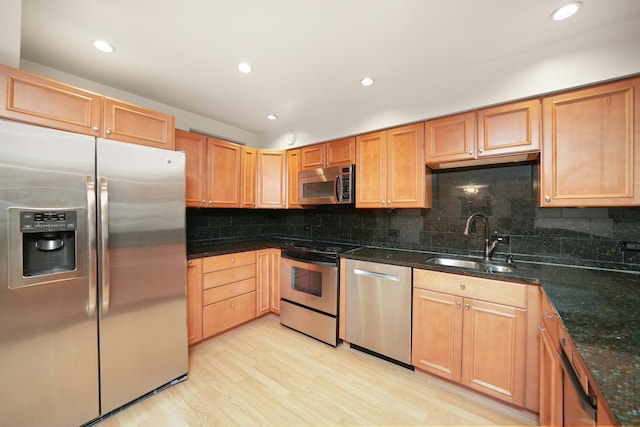 kitchen with sink, light hardwood / wood-style flooring, dark stone countertops, appliances with stainless steel finishes, and tasteful backsplash