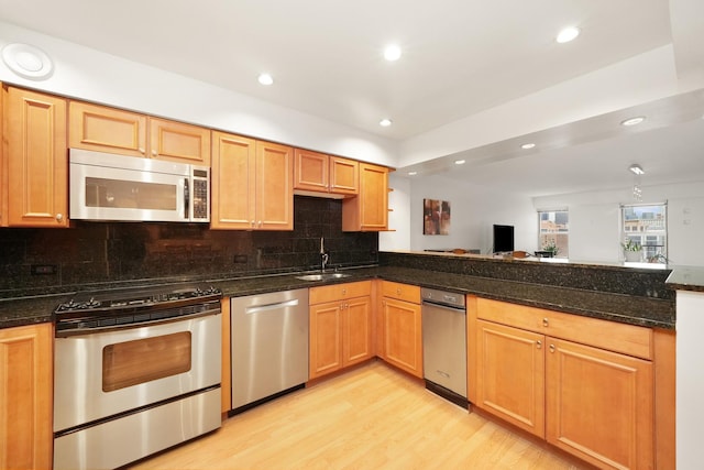 kitchen with backsplash, dark stone counters, sink, appliances with stainless steel finishes, and light hardwood / wood-style floors