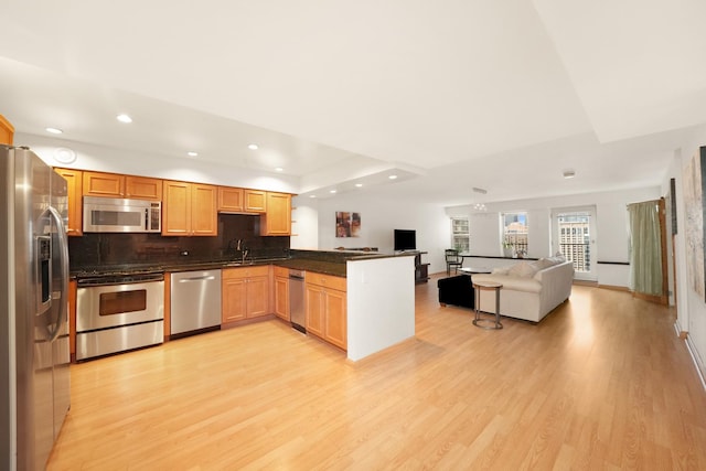 kitchen with sink, light wood-type flooring, appliances with stainless steel finishes, tasteful backsplash, and kitchen peninsula