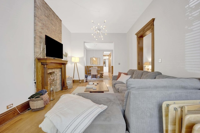 living room with a chandelier, light wood-type flooring, and a stone fireplace