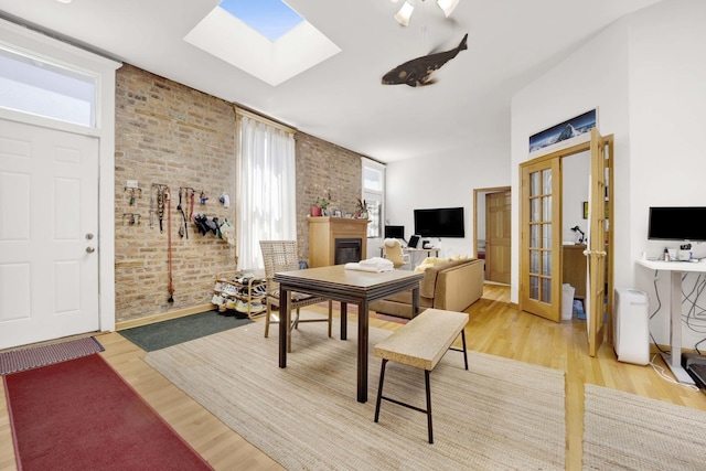 dining room featuring a skylight, french doors, brick wall, wood-type flooring, and a fireplace