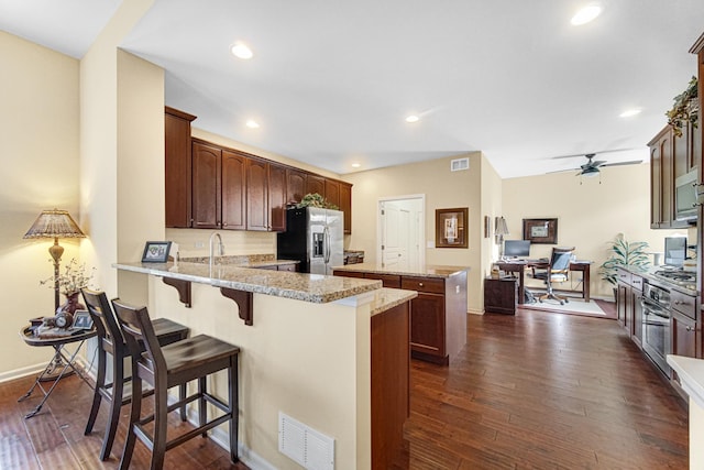 kitchen featuring ceiling fan, stainless steel appliances, light stone counters, dark hardwood / wood-style flooring, and kitchen peninsula