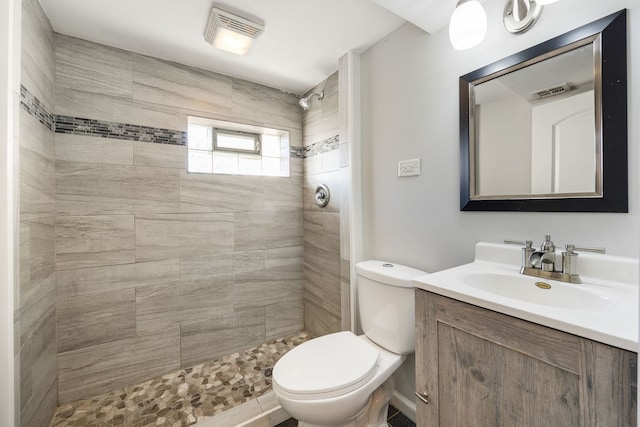 bathroom with a tile shower, vanity, and toilet