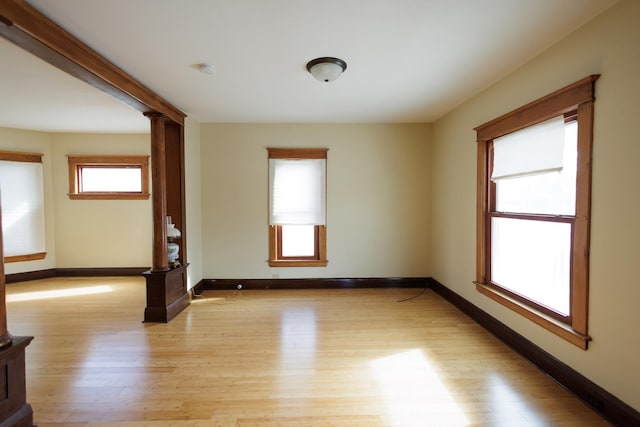 unfurnished room featuring light wood-type flooring and decorative columns