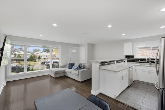 kitchen with dark wood-type flooring, stainless steel appliances, light stone counters, kitchen peninsula, and white cabinets