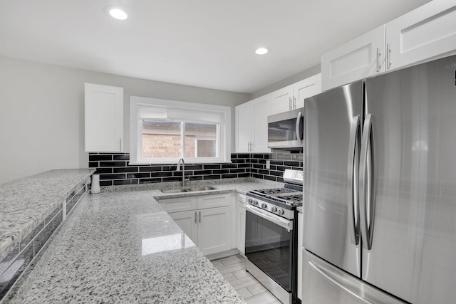 kitchen with white cabinets, sink, light stone countertops, tasteful backsplash, and stainless steel appliances