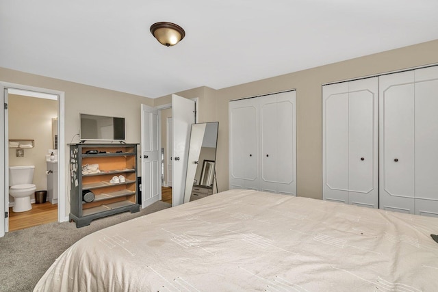 carpeted bedroom featuring ensuite bathroom and two closets