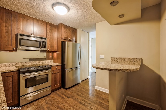 kitchen with dark hardwood / wood-style flooring, light stone counters, a textured ceiling, and appliances with stainless steel finishes