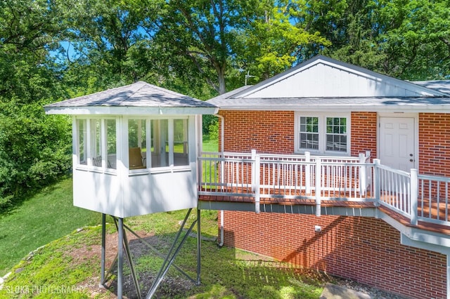 rear view of property featuring a sunroom, a wooden deck, and a lawn