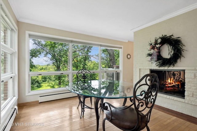 dining room featuring a brick fireplace, light hardwood / wood-style floors, ornamental molding, and a baseboard radiator