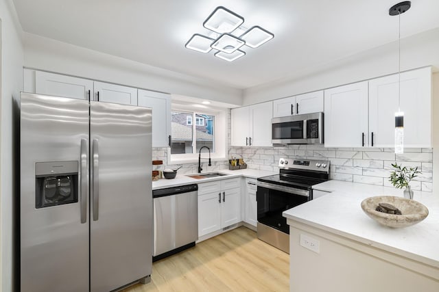 kitchen with sink, tasteful backsplash, decorative light fixtures, white cabinets, and appliances with stainless steel finishes