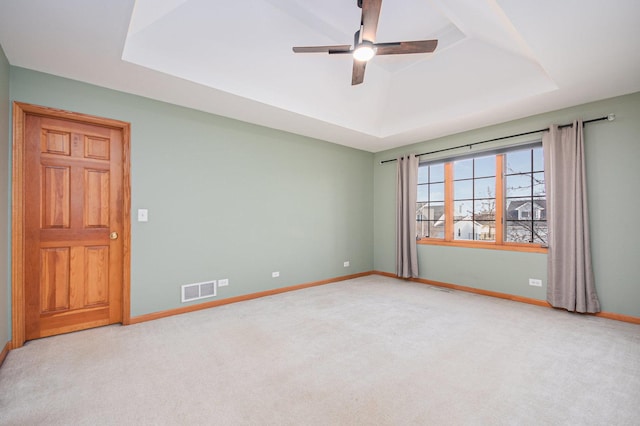 spare room with ceiling fan, light colored carpet, and a tray ceiling