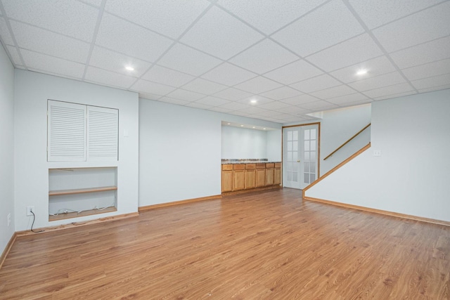 unfurnished living room with a paneled ceiling, french doors, and light hardwood / wood-style flooring