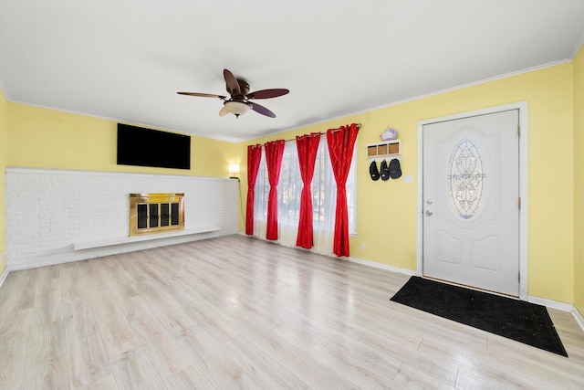 entryway featuring light wood-type flooring, ceiling fan, ornamental molding, and a fireplace