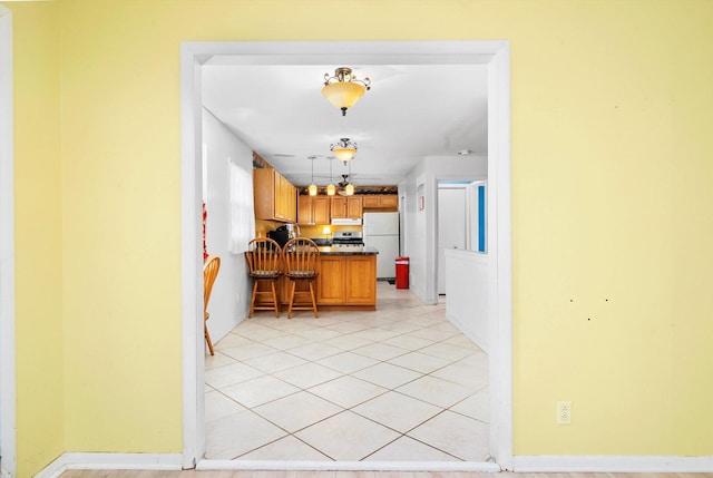 kitchen featuring kitchen peninsula, light tile patterned flooring, hanging light fixtures, white refrigerator, and a breakfast bar