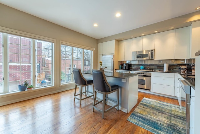 kitchen featuring white cabinets, a center island, light hardwood / wood-style flooring, a breakfast bar area, and appliances with stainless steel finishes