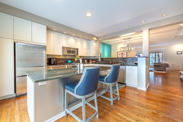 kitchen featuring a kitchen breakfast bar, light wood-type flooring, backsplash, pendant lighting, and appliances with stainless steel finishes