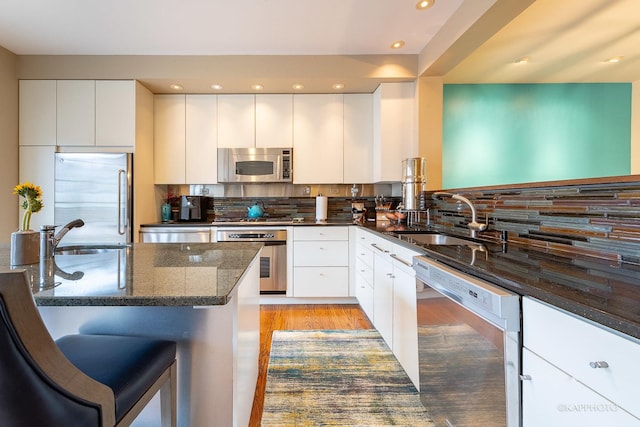 kitchen with appliances with stainless steel finishes, dark stone counters, white cabinets, and sink