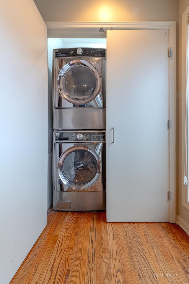 laundry room with light wood-type flooring and stacked washer / drying machine