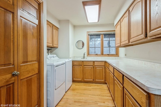 clothes washing area featuring light hardwood / wood-style floors, cabinets, washer and clothes dryer, and sink