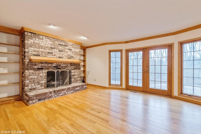 unfurnished living room featuring light wood-type flooring, french doors, crown molding, and a fireplace