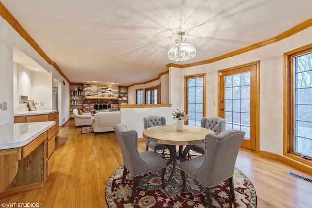 dining area featuring crown molding, light hardwood / wood-style floors, a brick fireplace, and an inviting chandelier