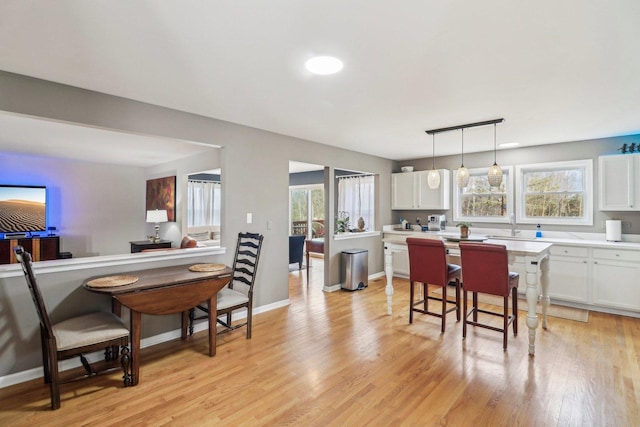 kitchen featuring a healthy amount of sunlight, light hardwood / wood-style flooring, hanging light fixtures, and white cabinets