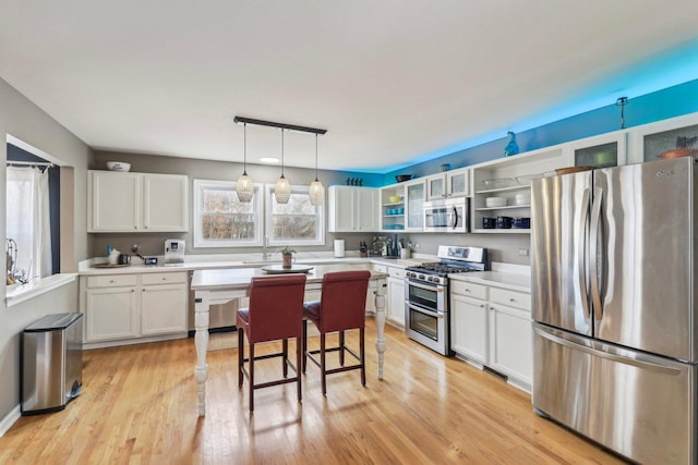 kitchen with a breakfast bar, white cabinetry, light hardwood / wood-style flooring, appliances with stainless steel finishes, and pendant lighting