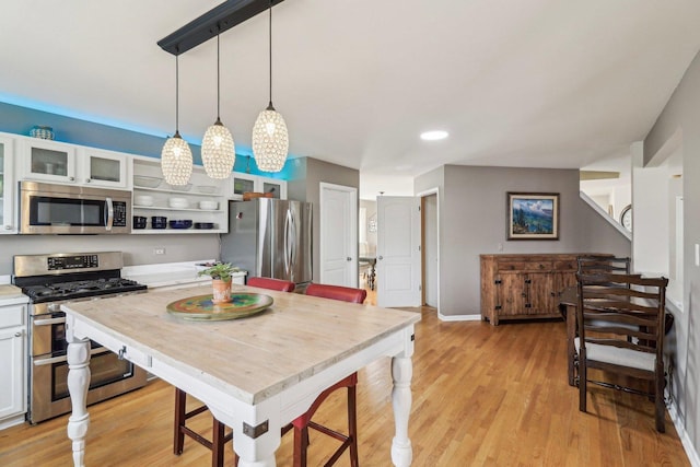 kitchen featuring appliances with stainless steel finishes, decorative light fixtures, light hardwood / wood-style floors, and white cabinets