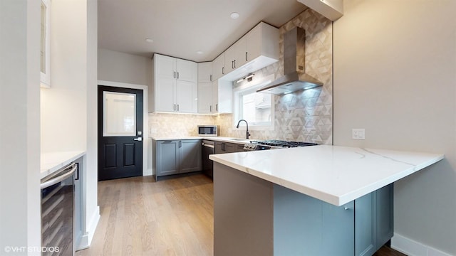 kitchen with kitchen peninsula, backsplash, wall chimney exhaust hood, gray cabinets, and wine cooler