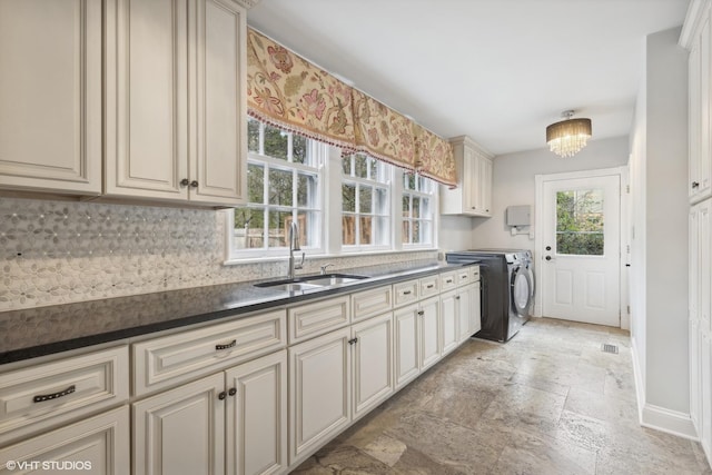 clothes washing area with washer and dryer, a chandelier, cabinets, and sink