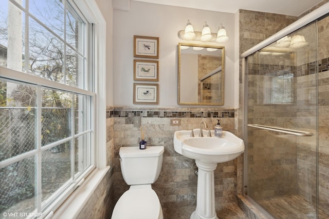 bathroom featuring walk in shower, toilet, tile walls, and a healthy amount of sunlight